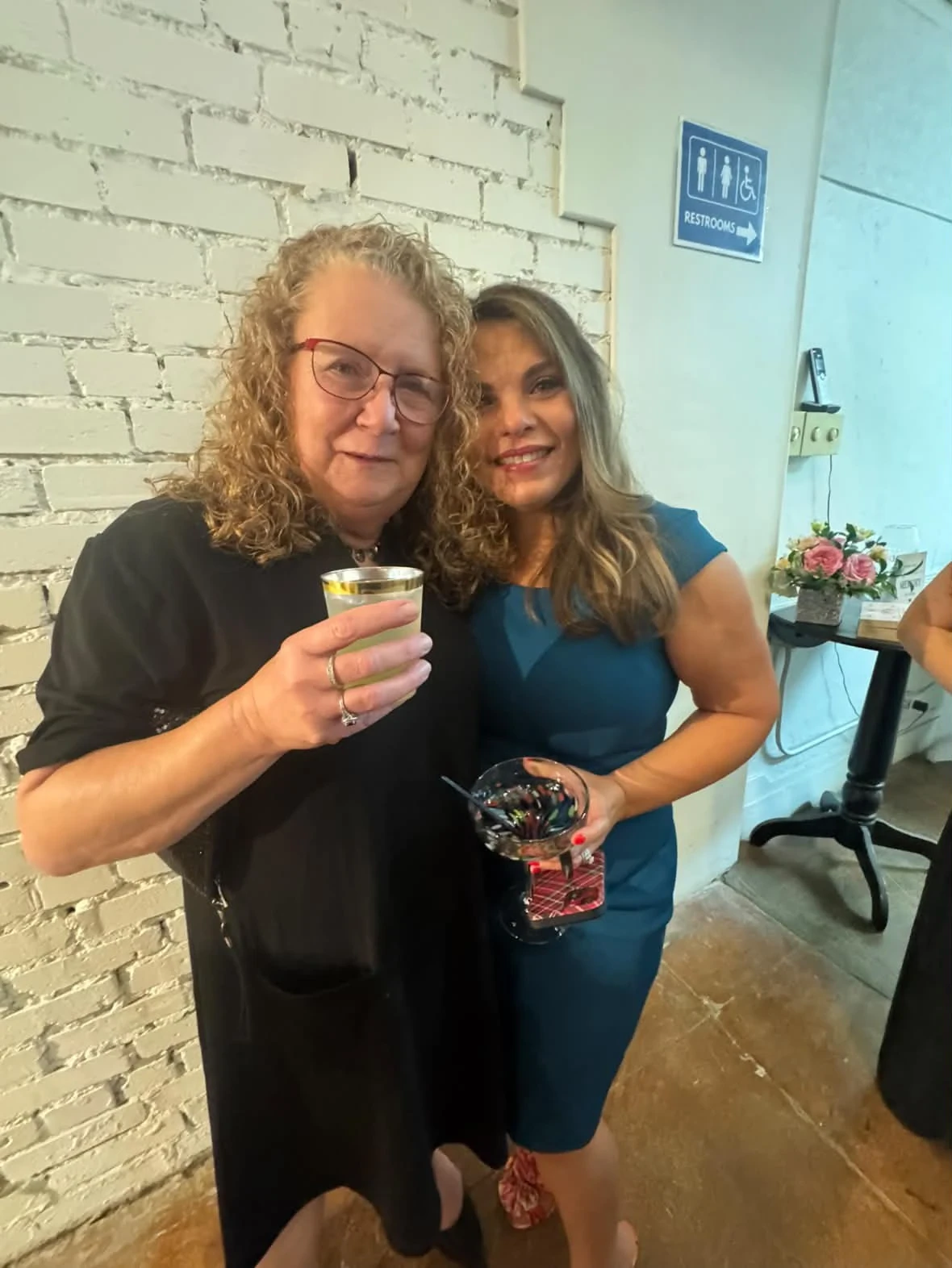 Angela and a guest smiling together while holding their drinks.