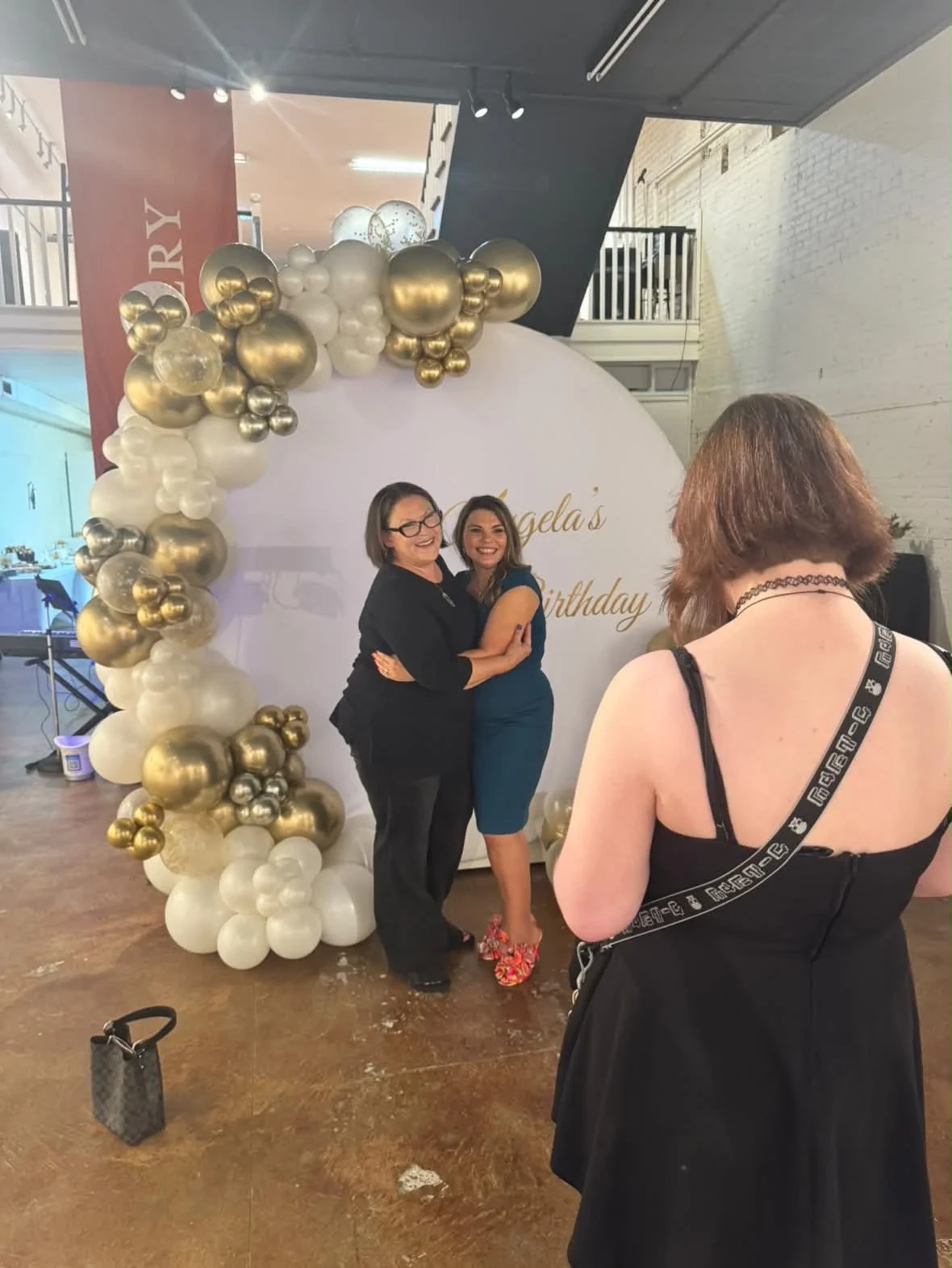 Two women posing at the birthday backdrop while a guest takes their photograph.