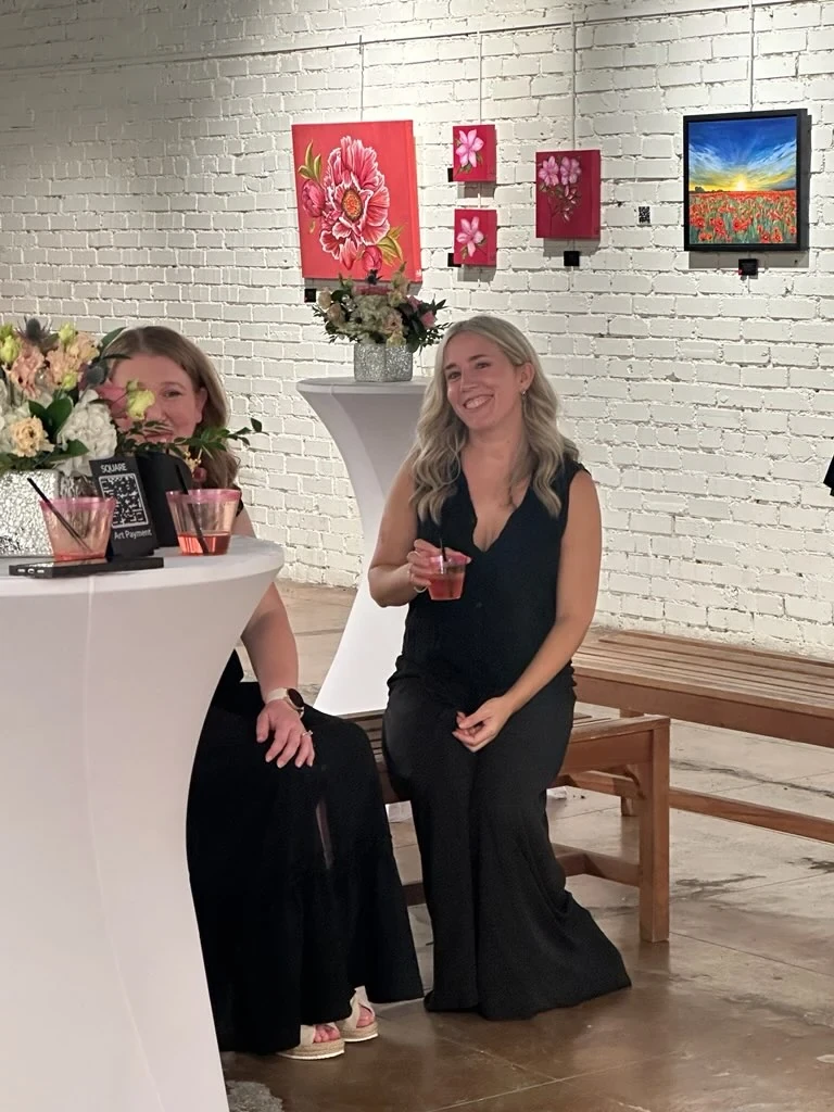 Two guests seated beside a cocktail table and colorful flower paintings.