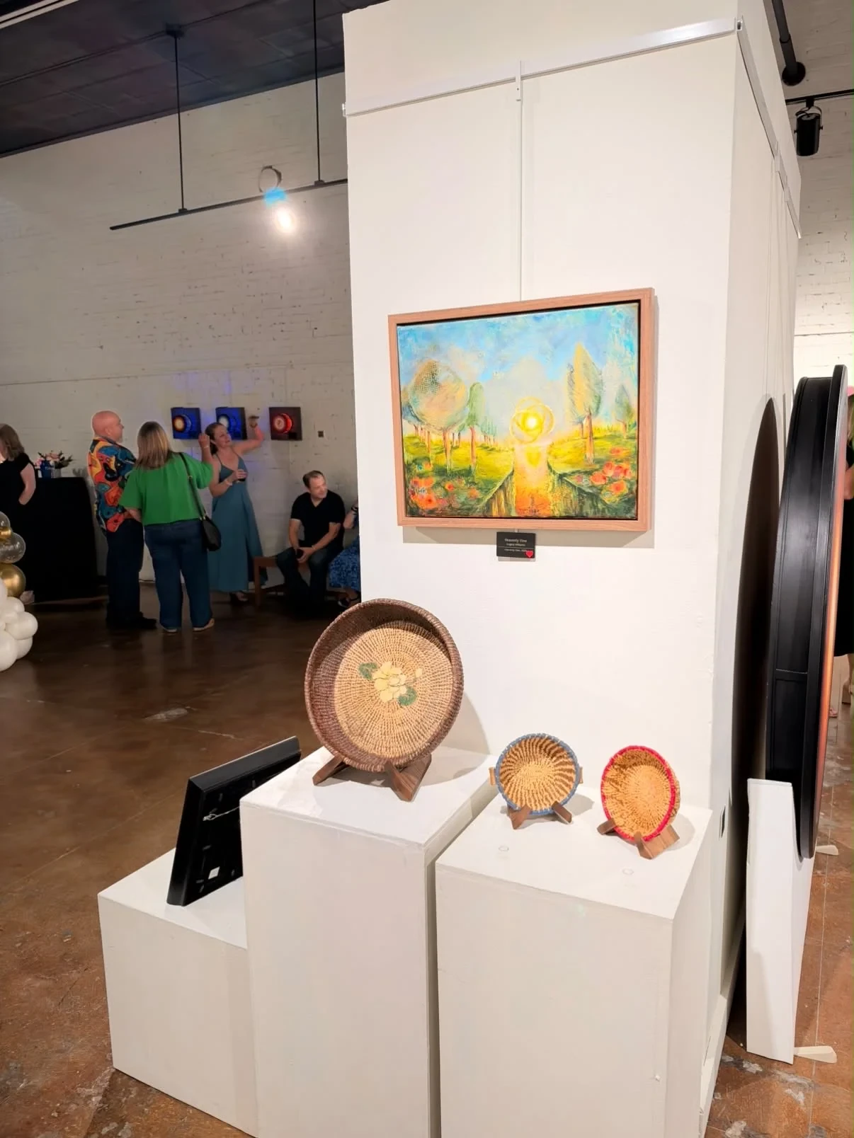 A sunlit landscape painting displayed above three woven baskets.