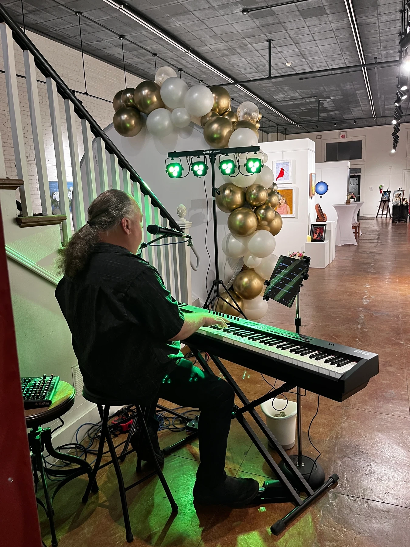 A musician playing a keyboard and singing beside the gallery stairs.