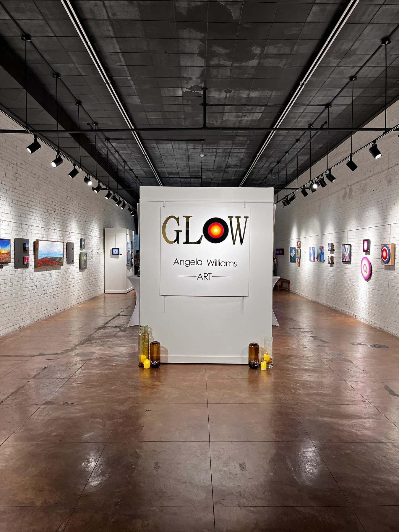 The GLOW exhibition sign centered between walls of paintings before guests arrive.