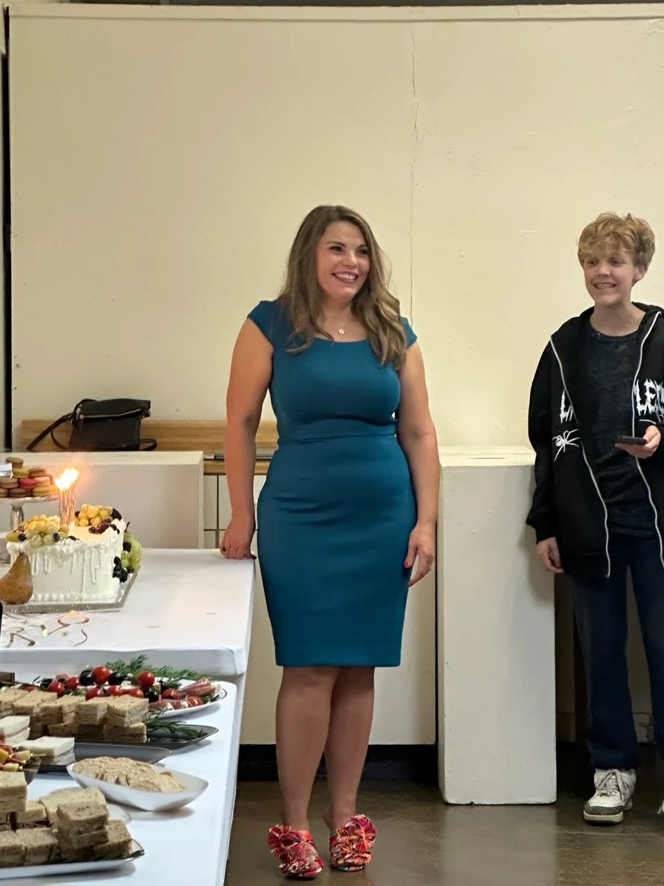 Angela standing beside a young guest and a birthday cake with lit candles.
